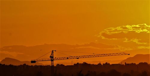 Silhouette cranes at construction site during sunset