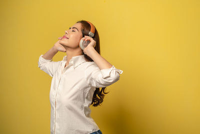 Young woman looking away while standing against yellow background