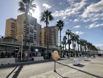 People on street by palm trees and buildings in city against sky