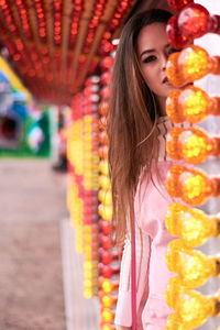 Portrait of female model standing amidst illuminated light bulbs at amusement park