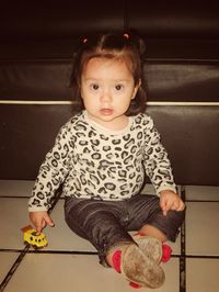 Portrait of cute girl sitting with toy car on floor at home