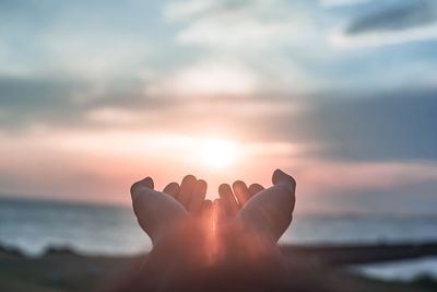 Person hand against sea during sunset