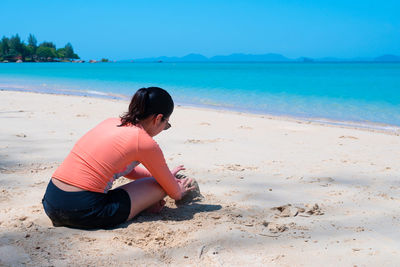 Woman sitting on shore at beach against sky