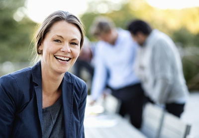 Portrait of businesswoman laughing at patio with colleagues in background