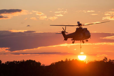 Silhouette helicopter flying against sky during sunset