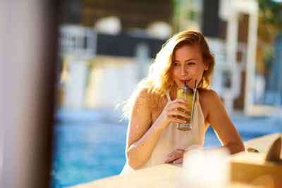 Woman drinking juice against swimming pool