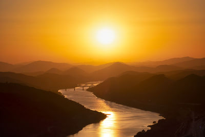 Scenic view of river and silhouette mountains against the orange sky