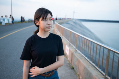 Teenage girl looking away while standing against railing