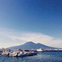 Boats moored in sea against clear blue sky