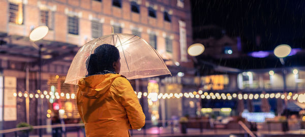 Rear view of woman standing with umbrella in city at night