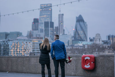 Rear view of woman with arms outstretched against cityscape