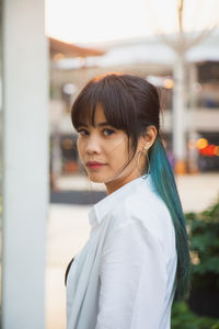 Asian woman in a white shirt with multi colour long hair, looking at a camera with urban background