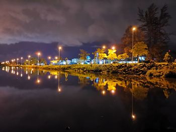 Illuminated city by lake against sky at night