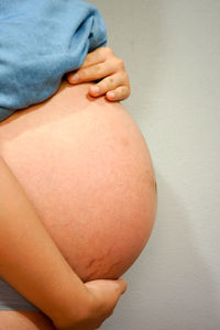 Midsection of pregnant woman in nightwear standing against wall