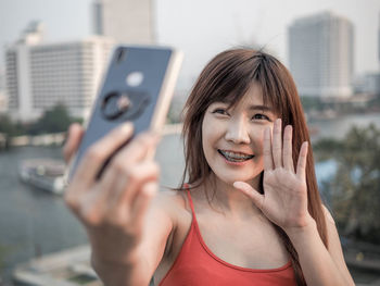 Portrait of a smiling young woman using mobile phone in city