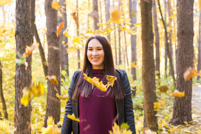 Smiling young woman standing in forest during autumn