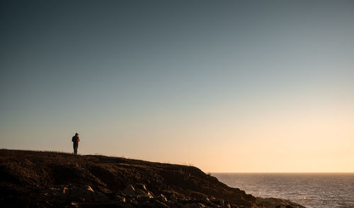 Man standing on rock by sea against clear sky