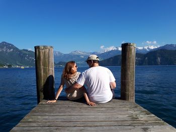 Couple sitting on pier over lake against sky