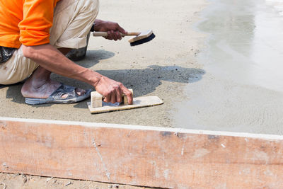 Midsection of man leveling wet cement with tool