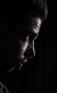 Side view of young man sweating against black background