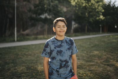 Portrait of smiling boy standing in park in summer