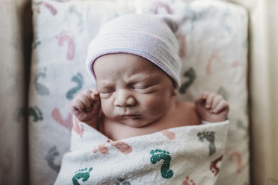Overhead view of newborn boy with hat swaddled in hospital bassinet