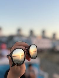 Close-up of hand holding eyeglasses against sky