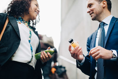 Low angle view of smiling business colleagues standing with drink bottles in city