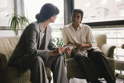 Businesswoman discussing over placard with non-binary colleague while sitting at office