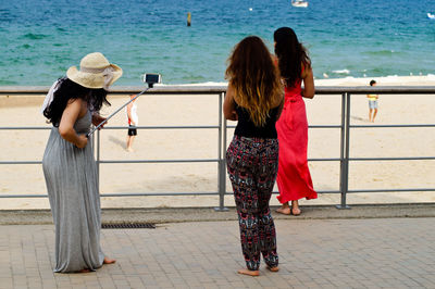 Full length of woman with friends taking selfie at beach