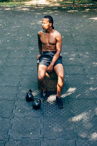 Full length of shirtless man sitting on footpath