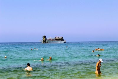 People swimming in sea against clear sky