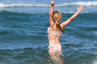 Rear view of girl with arms raised standing in sea