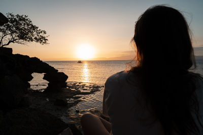 Woman looking at sea against sky during sunset