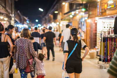 Rear view of people walking on illuminated city at night