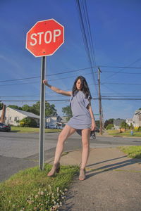 Full length of woman holding stop sign while standing in city against blue sky