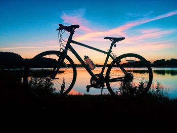 Silhouette bicycle by lake against sky during sunset