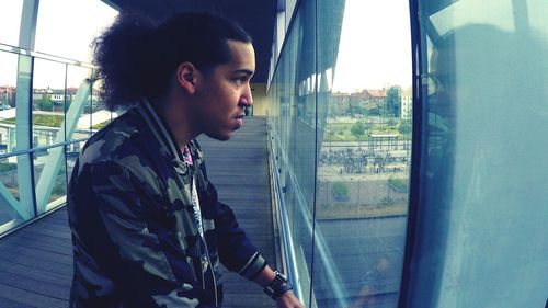 Side view of young man looking away while standing on footbridge in city