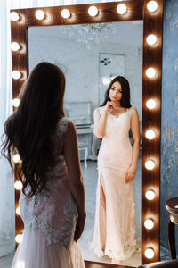 Rear view of bride standing in front of illuminated mirror