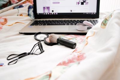 Laptop and beauty product on bed at home