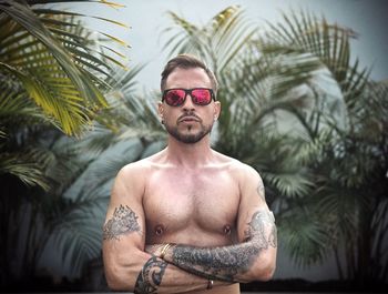 Portrait of young man wearing sunglasses standing against palm tree