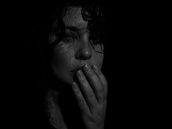 Portrait of young woman crying against black background