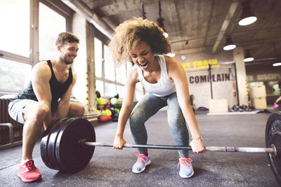 Young woman with training partner preparing to lift barbell in gym