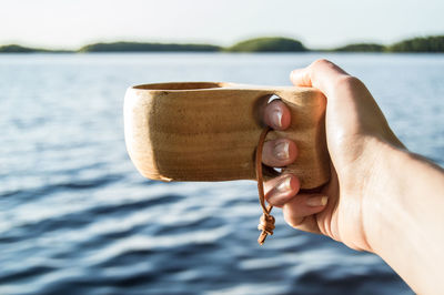 Close-up of hand holding wooden cup over seascape
