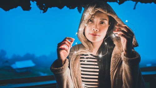Portrait of woman holding illuminated string lights at night