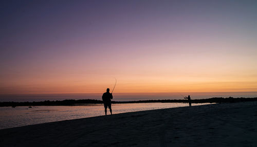Silhouette people standing on beach against sky during sunset