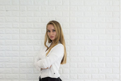 Portrait of young businesswoman standing against white brick wall