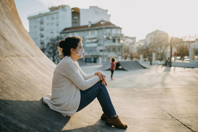 Side view of woman wearing mask sitting against building