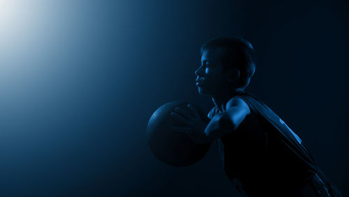 Side view of boy playing with ball against black background