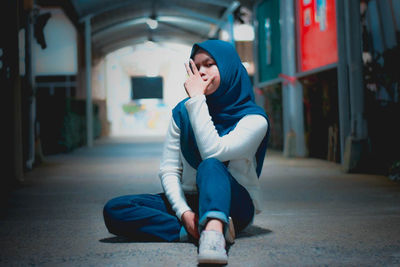 Portrait of young woman wearing hijab sitting outdoors at night